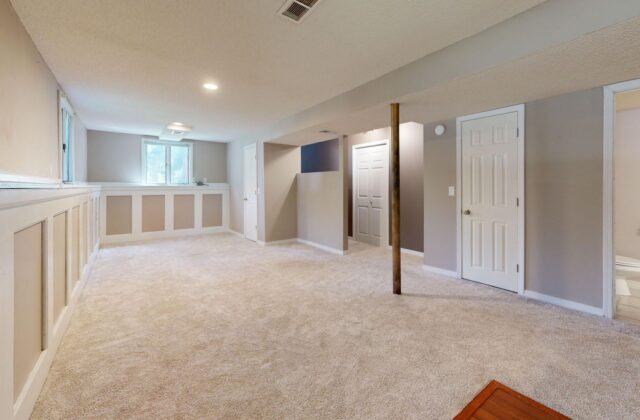 White portable dehumidifier running in a finished basement with hardwood shelving and a small hygrometer nearby