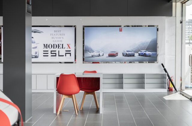 Row of new electric vehicles parked inside a modern car dealership showroom with large windows