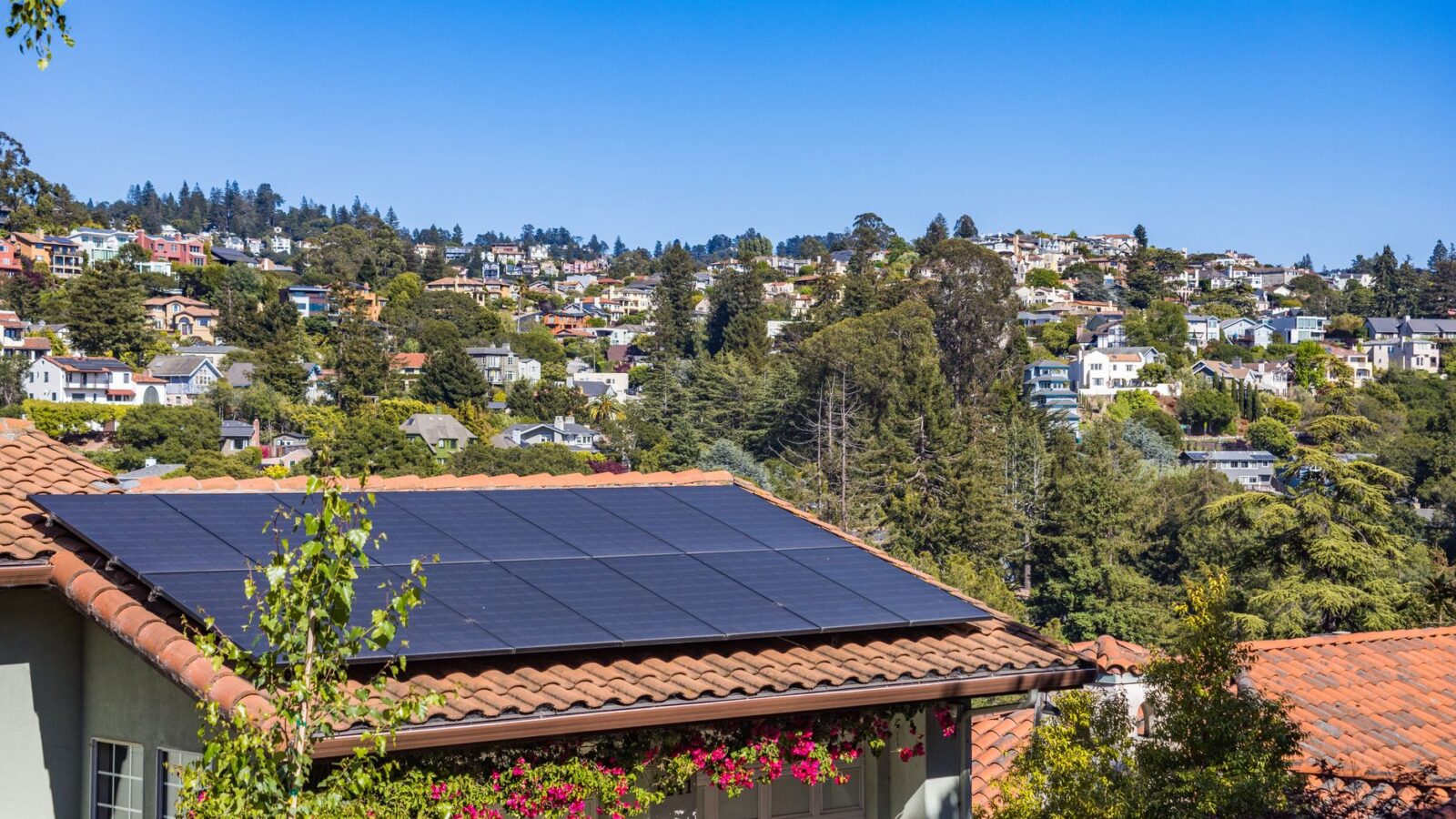 Rows of black monocrystalline solar panels installed on a residential asphalt-shingle roof under a partly cloudy sky