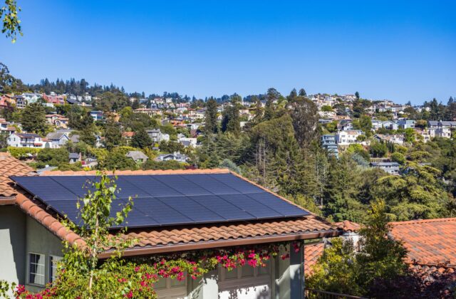 Rows of black monocrystalline solar panels installed on a residential asphalt-shingle roof under a partly cloudy sky