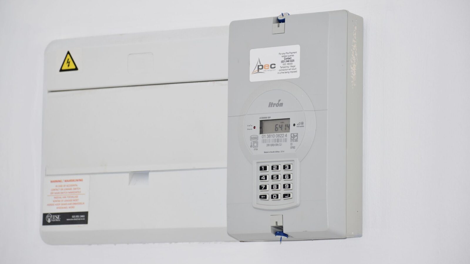 Close up of a residential electricity meter mounted on a house exterior next to a paper utility bill