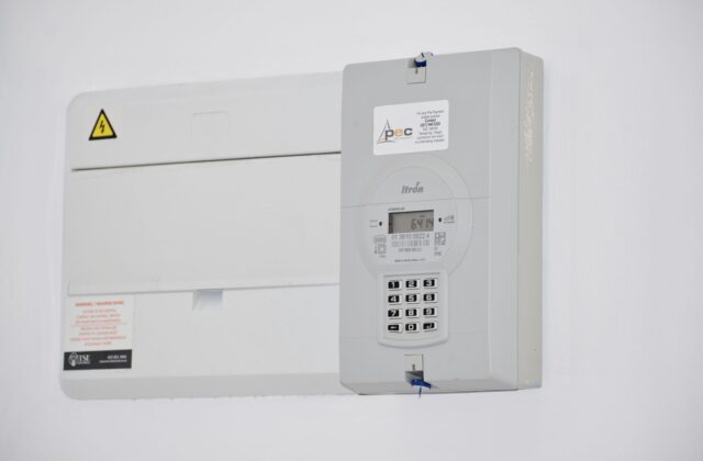Close up of a residential electricity meter mounted on a house exterior next to a paper utility bill