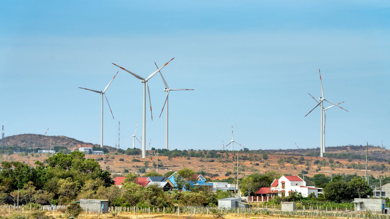 Small residential wind turbine on tall monopole in a rural backyard with neighboring houses visible in the distance